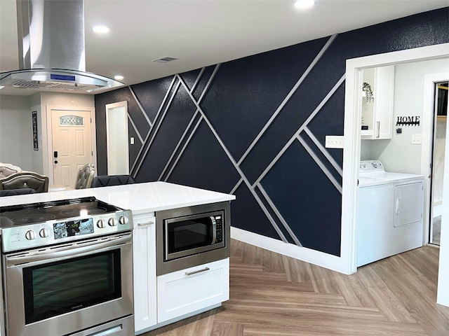 kitchen with washer and dryer, island exhaust hood, stainless steel appliances, light countertops, and white cabinetry