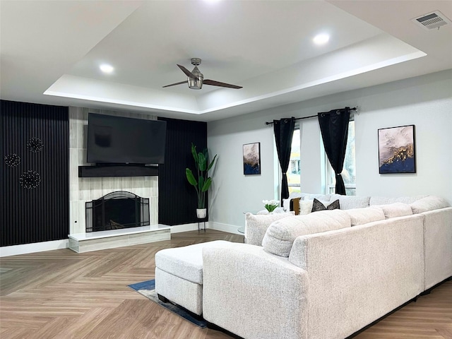 living room with visible vents, a fireplace with raised hearth, baseboards, and a tray ceiling