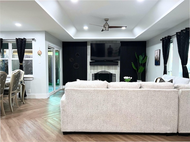 living room with a raised ceiling, a ceiling fan, recessed lighting, a fireplace, and baseboards