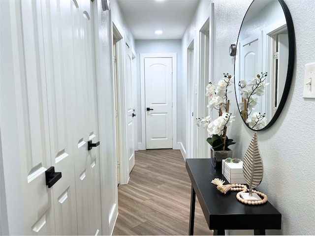 hallway featuring baseboards, wood finished floors, and a textured wall