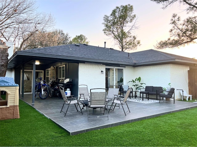 back of property with outdoor lounge area, a patio area, brick siding, and roof with shingles