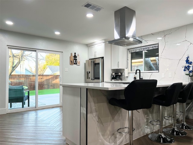 kitchen featuring visible vents, island exhaust hood, a breakfast bar area, stainless steel fridge with ice dispenser, and light countertops