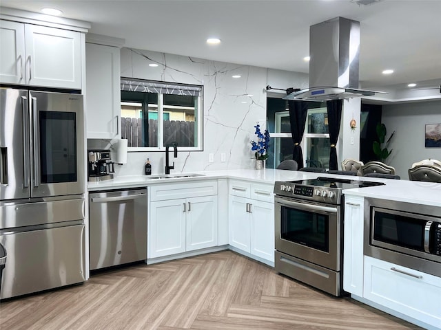 kitchen featuring a sink, appliances with stainless steel finishes, white cabinets, island range hood, and light countertops