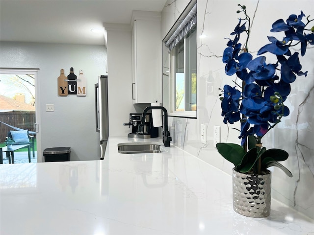 kitchen with a sink, light stone countertops, white cabinets, and freestanding refrigerator