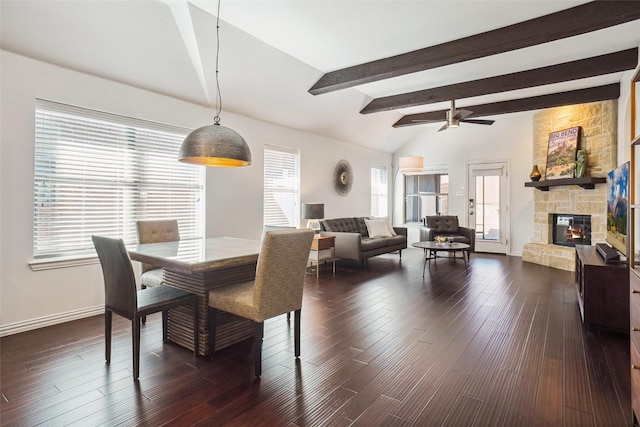 dining room with vaulted ceiling with beams, dark wood-type flooring, baseboards, ceiling fan, and a stone fireplace