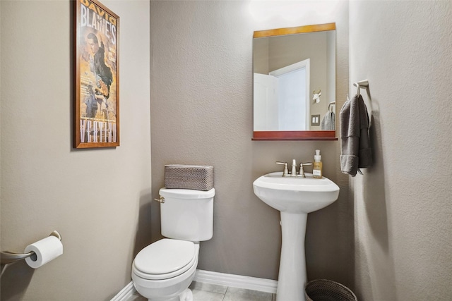 half bath with tile patterned flooring, toilet, and baseboards