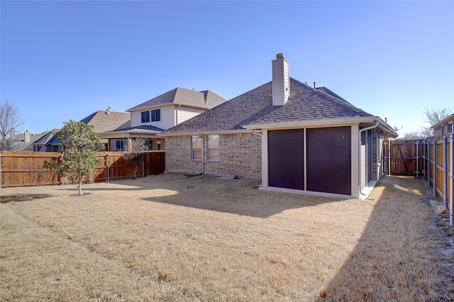 back of property with a fenced backyard, brick siding, and a chimney