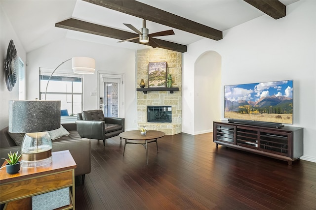 living area featuring lofted ceiling with beams, a stone fireplace, wood finished floors, and ceiling fan