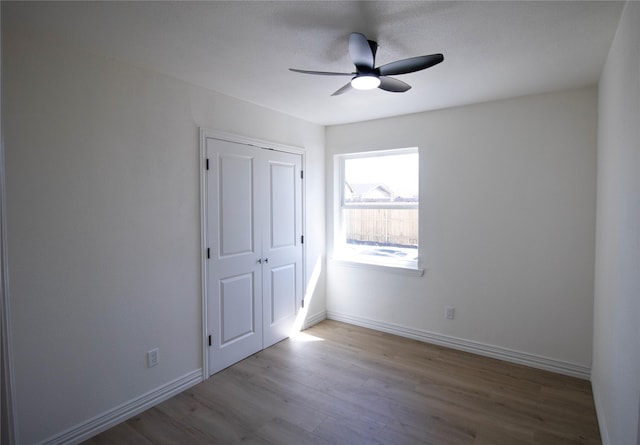 unfurnished bedroom featuring a ceiling fan, wood finished floors, baseboards, and a closet