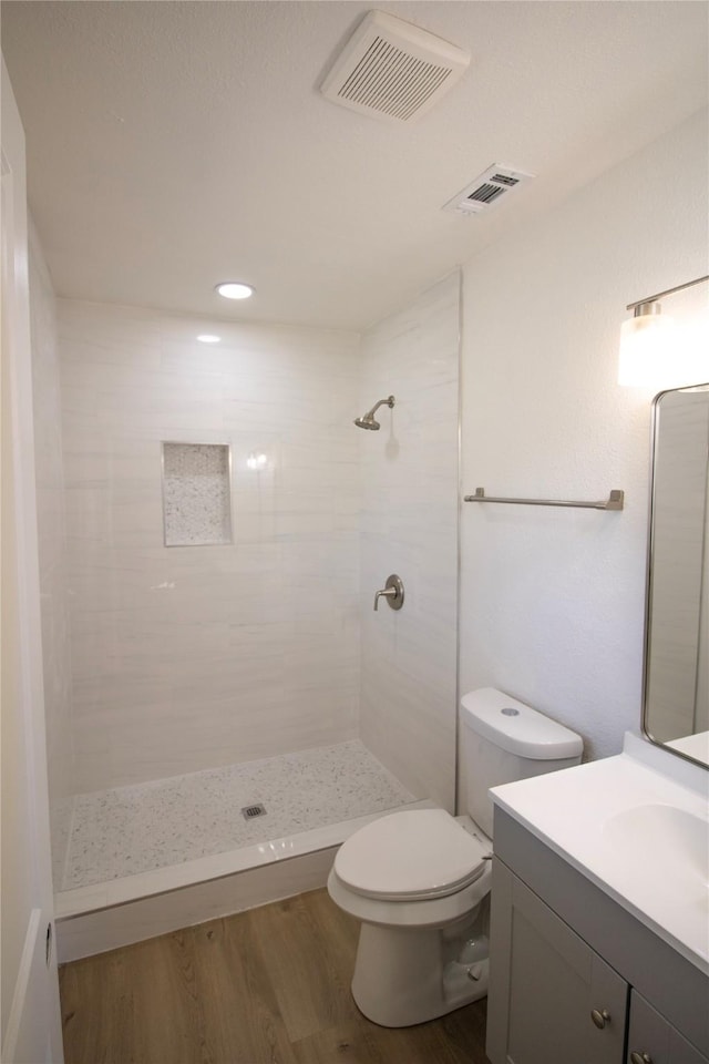 full bathroom featuring a tile shower, visible vents, toilet, and wood finished floors