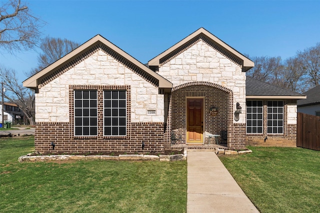 french provincial home with fence, roof with shingles, a front lawn, stone siding, and brick siding