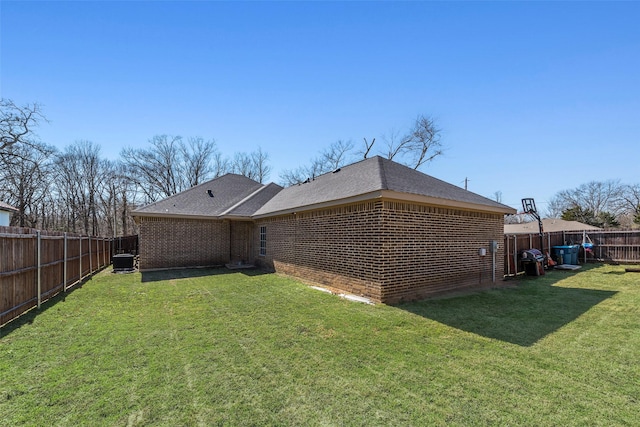 rear view of property featuring brick siding, central AC unit, a fenced backyard, and a lawn