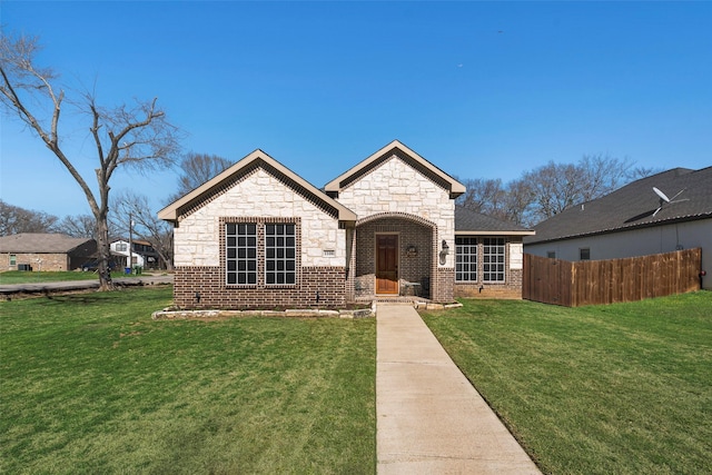 french provincial home featuring brick siding, a front lawn, and fence