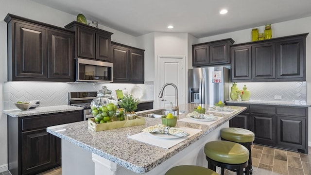 kitchen with a kitchen island with sink, appliances with stainless steel finishes, a breakfast bar, and a sink