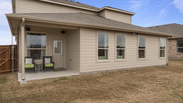 rear view of house featuring a patio area, fence, a lawn, and a shingled roof