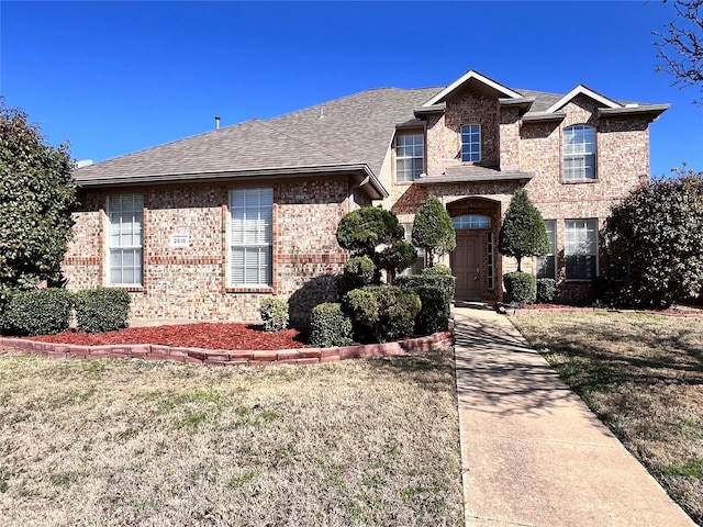 traditional home with a front lawn, brick siding, and a shingled roof