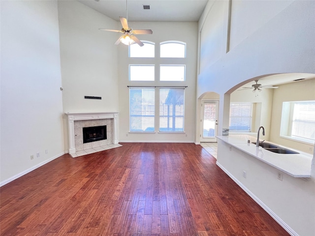 unfurnished living room featuring a tile fireplace, arched walkways, dark wood-style floors, a ceiling fan, and a sink