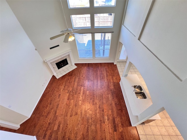 unfurnished living room with a ceiling fan, wood finished floors, baseboards, a tile fireplace, and a towering ceiling