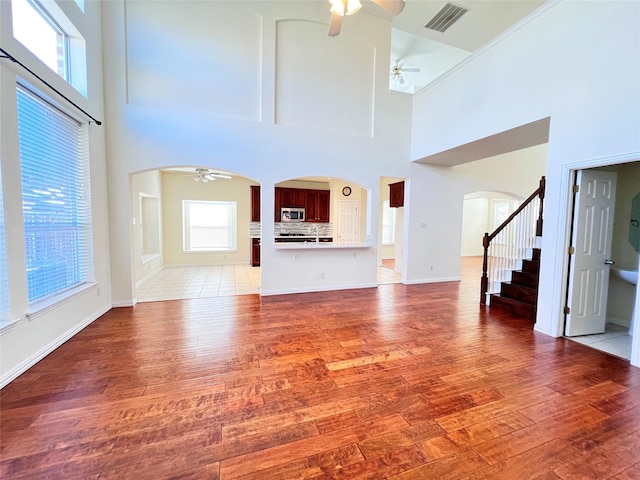 unfurnished living room with visible vents, ceiling fan, stairway, light wood-style flooring, and arched walkways