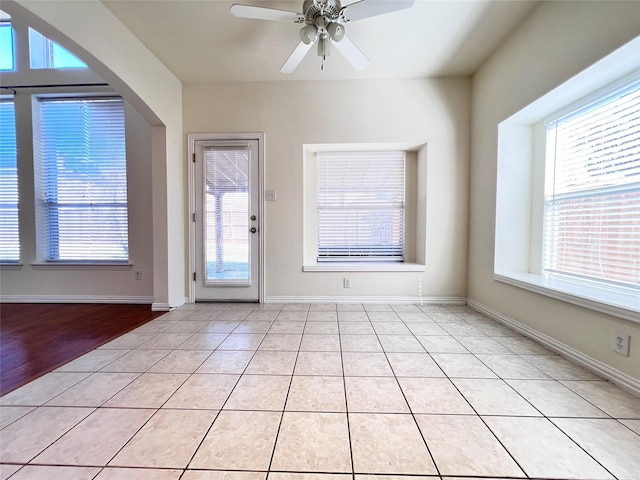 interior space with light tile patterned floors, baseboards, arched walkways, and ceiling fan