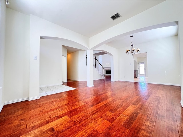 unfurnished living room with visible vents, hardwood / wood-style flooring, arched walkways, an inviting chandelier, and baseboards