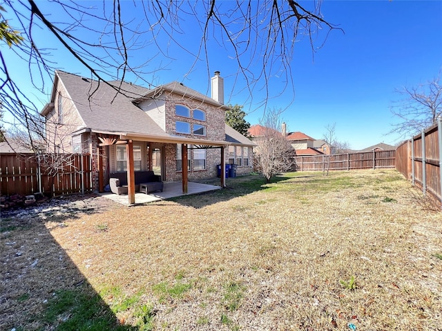 back of property with a lawn, a fenced backyard, brick siding, a chimney, and a patio area