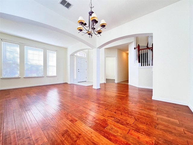 unfurnished room featuring visible vents, wood-type flooring, arched walkways, baseboards, and a chandelier