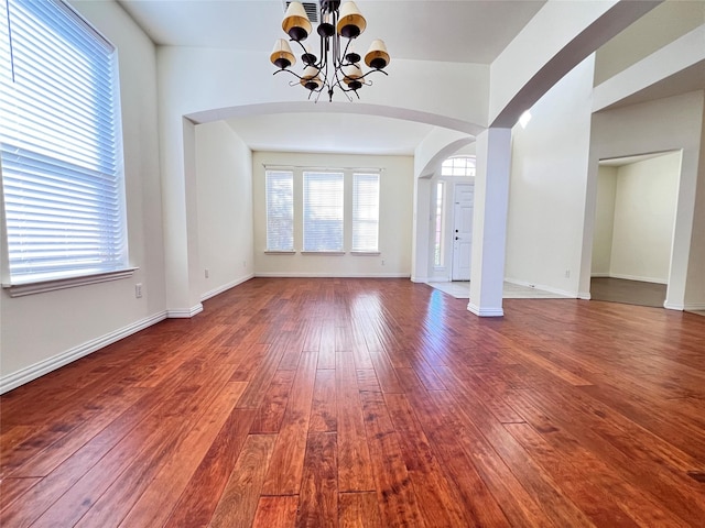 interior space with a chandelier, arched walkways, baseboards, and hardwood / wood-style flooring