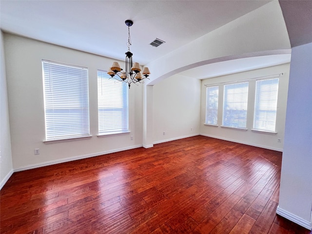 unfurnished room with dark wood-type flooring, a wealth of natural light, and a chandelier