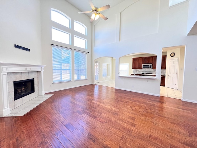 unfurnished living room with baseboards, light wood-type flooring, a fireplace, arched walkways, and a ceiling fan