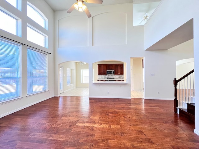 unfurnished living room with arched walkways, stairway, a ceiling fan, and wood finished floors