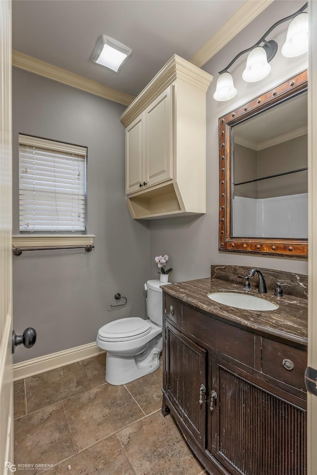 bathroom with toilet, stone finish flooring, crown molding, baseboards, and vanity