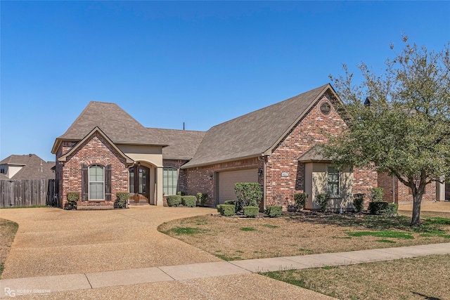 french country home featuring fence, brick siding, an attached garage, and a shingled roof