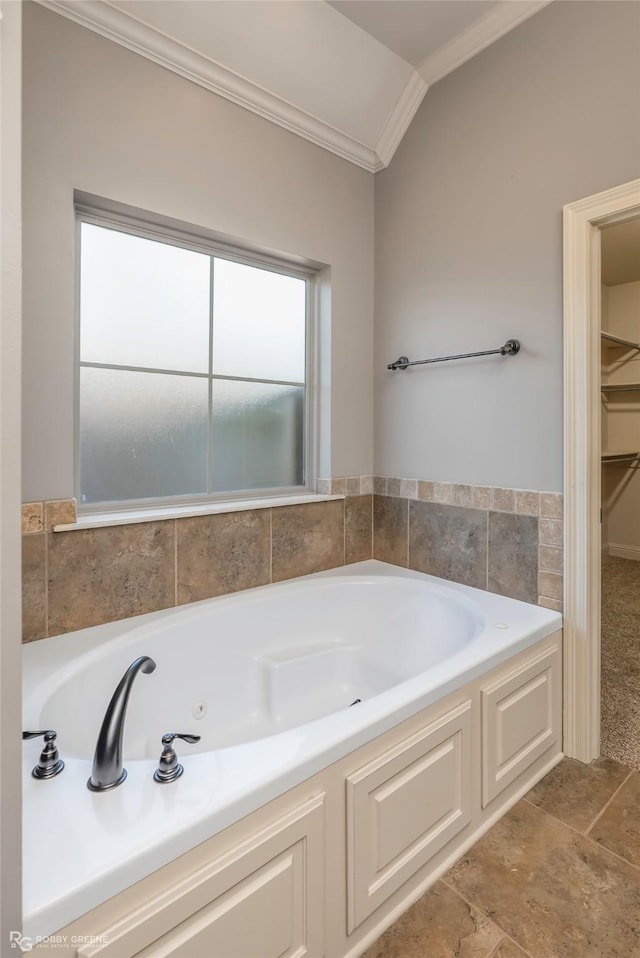 bathroom featuring a walk in closet, a garden tub, crown molding, and vaulted ceiling