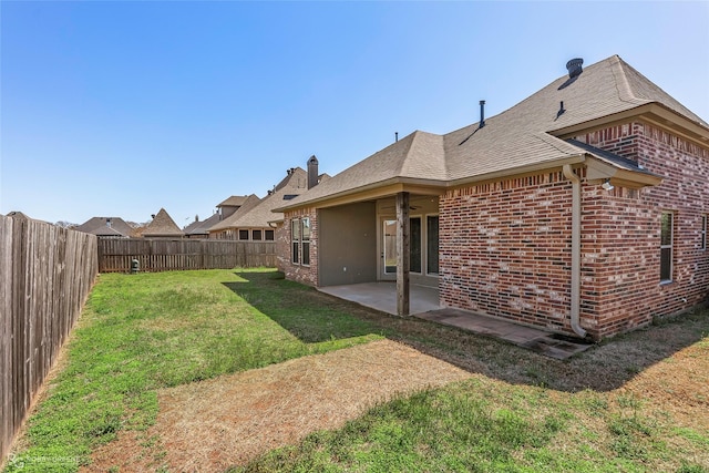 back of house with brick siding, a shingled roof, a lawn, a fenced backyard, and a patio area