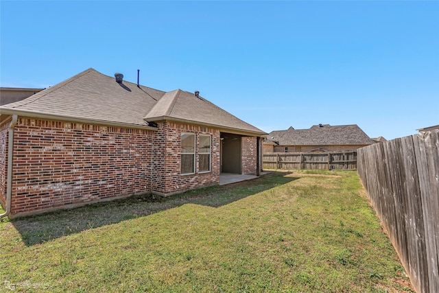 back of property featuring brick siding, roof with shingles, a yard, a fenced backyard, and a patio