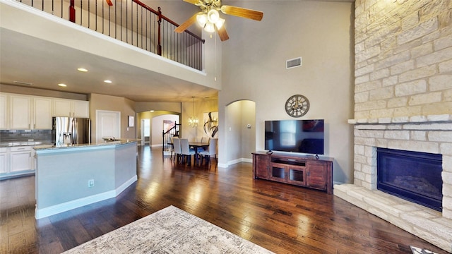 living area with visible vents, a ceiling fan, dark wood-style floors, arched walkways, and a stone fireplace