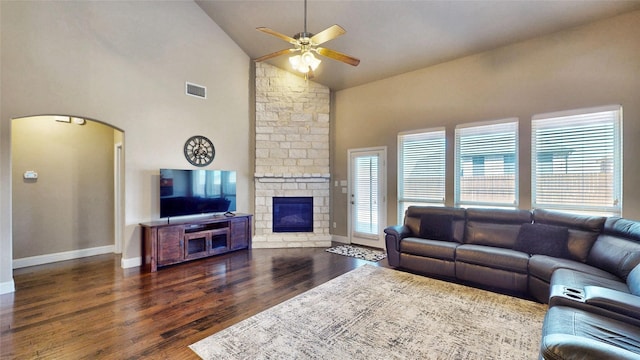 living area featuring wood finished floors, visible vents, arched walkways, ceiling fan, and a stone fireplace