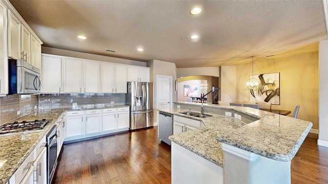 kitchen featuring visible vents, dark wood-style floors, arched walkways, appliances with stainless steel finishes, and a large island with sink