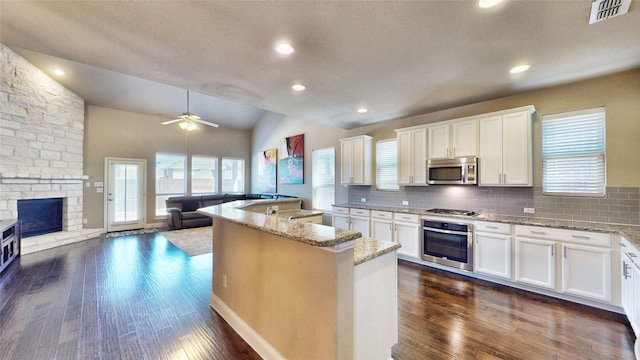 kitchen with visible vents, open floor plan, dark wood-style floors, stainless steel appliances, and a stone fireplace