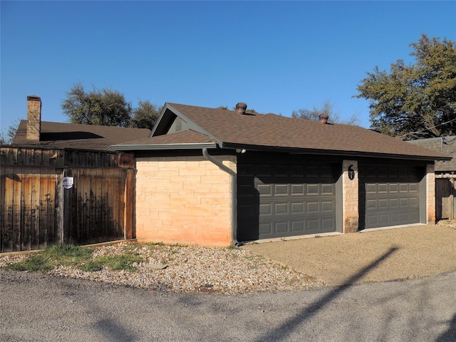 view of property exterior with a shingled roof, a garage, and fence