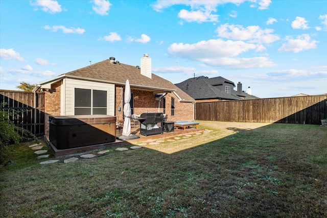 rear view of house with a chimney, a lawn, a hot tub, and a fenced backyard