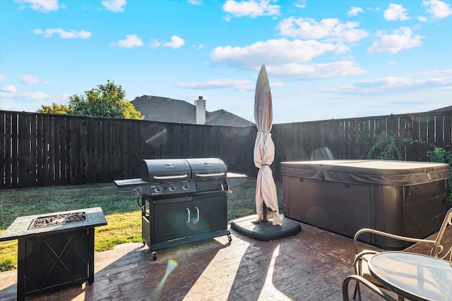 view of patio with area for grilling, a hot tub, a fenced backyard, and an outdoor fire pit