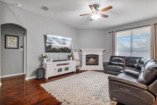 living room featuring ceiling fan, baseboards, a lit fireplace, arched walkways, and wood-type flooring