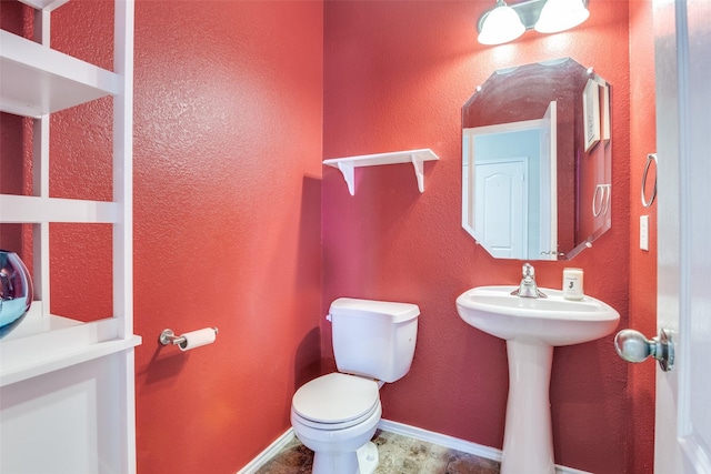 half bathroom featuring toilet, baseboards, and a sink