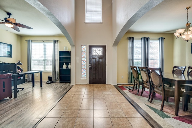 tiled entrance foyer with ceiling fan with notable chandelier, baseboards, and arched walkways