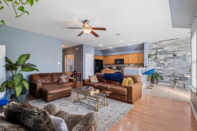 living area featuring visible vents, light wood-style floors, ceiling fan, and an accent wall