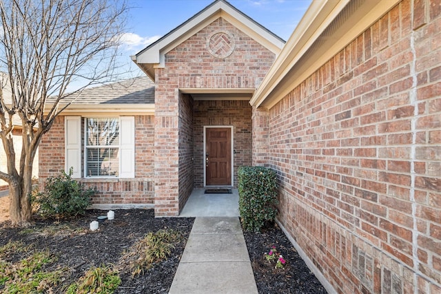 doorway to property featuring brick siding and a shingled roof