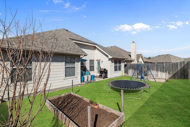 rear view of property featuring a trampoline, roof with shingles, a yard, a fenced backyard, and a vegetable garden