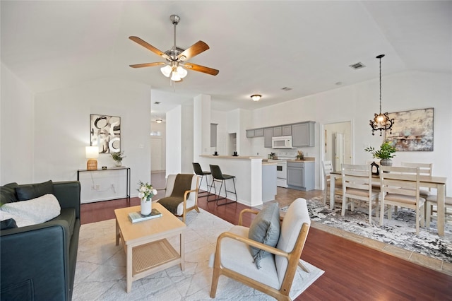 living room featuring visible vents, ceiling fan with notable chandelier, wood finished floors, and vaulted ceiling